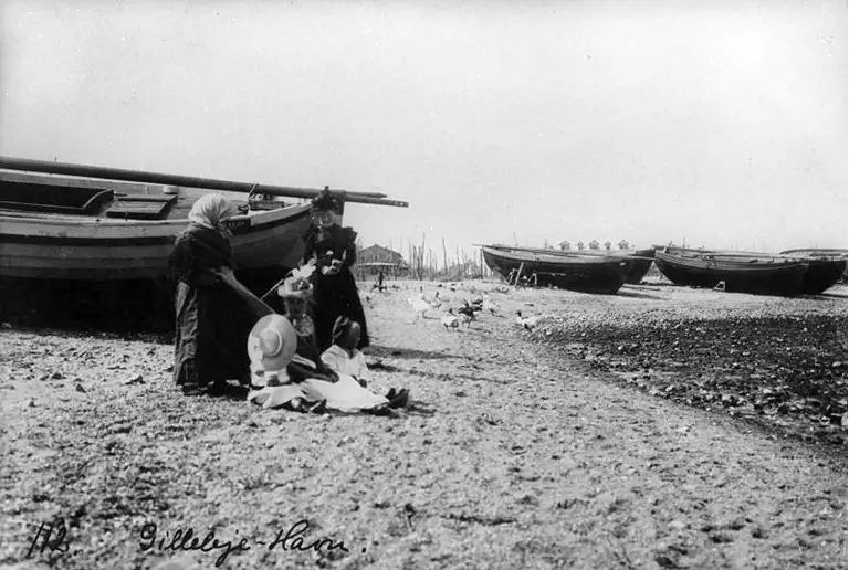 En fiskerkone taler med sommergæster ved den nordlige ende af Gilleleje Havn. Billedet er taget på et tidspunkt mellem 1896 og 1910. 