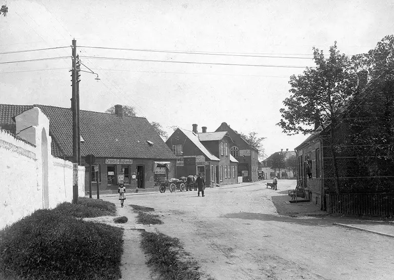 Jævnstrøms-luftledningsanlæg på træmaster og med glødepærer som gadebelysning. Græsted Hovedgade 1, ca. 1922